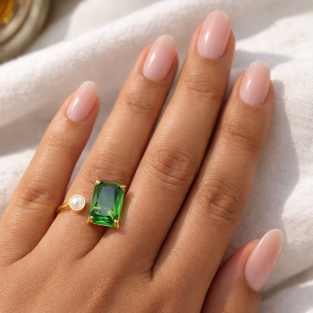 Hand wearing a gold ring with a green gemstone on a light background