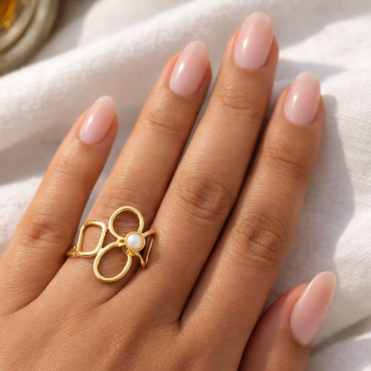 Hand wearing a gold ring with a pearl on a light background