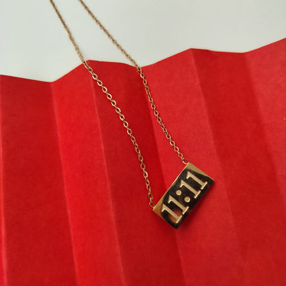 A rose gold pendant with the number 11:11 on it, displayed on a red textured surface, attached to a chain.