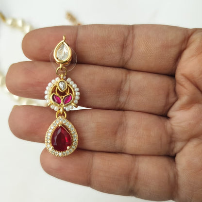 Gold earring with red and clear gemstones held between fingers on a white background