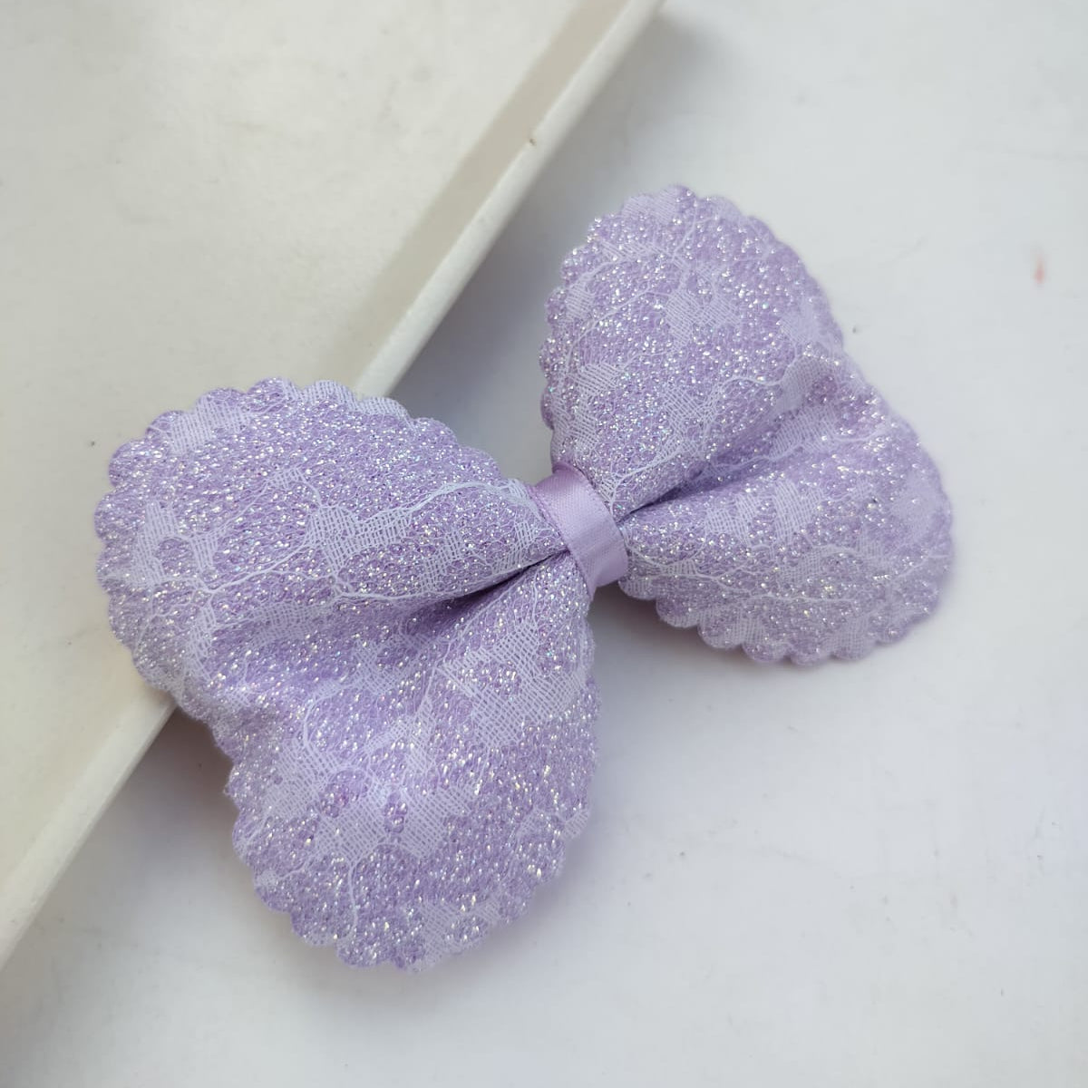 Purple glittery bow on a white surface with a white box in the background
