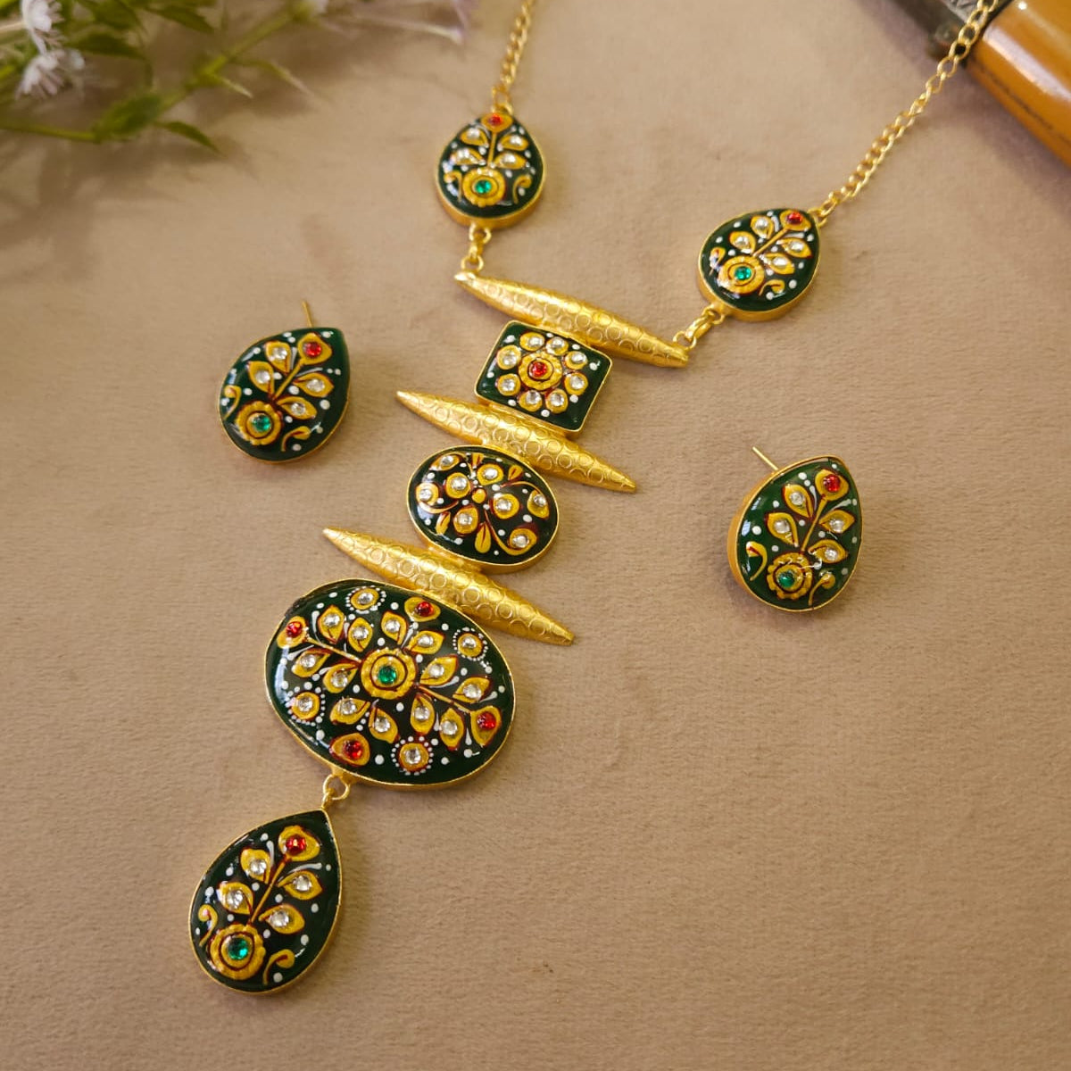 Gold necklace with green and red gemstones on a beige surface